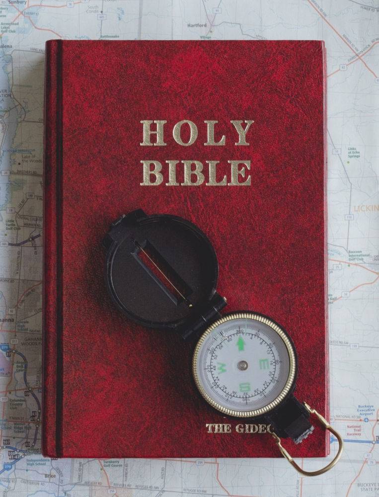 A compass and bible on top of a map.