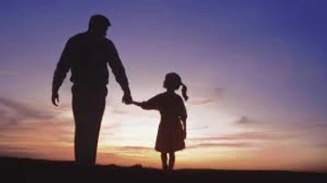 A man and child holding hands at sunset.