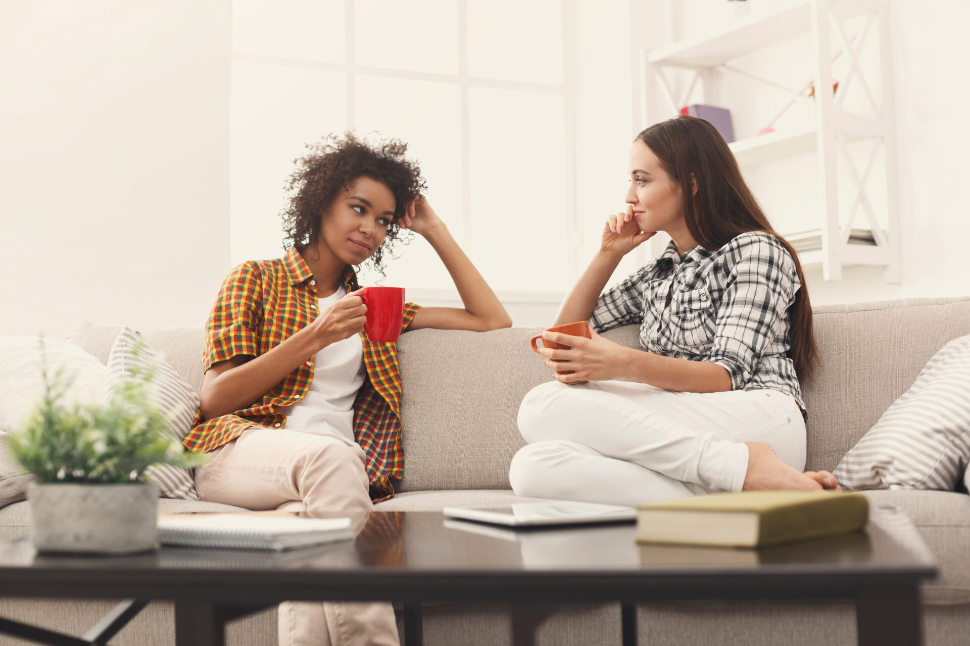 Two women sitting on a couch drinking coffee.